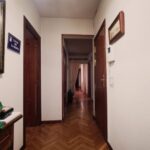 Chodba s tmavou drevenou parketovou podlahou, bielymi stenami, hnedými dverami a masívnym zrkadlom v ráme.