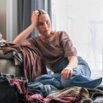 Nešťastná žena sedí na zemi pri kope vyhádzaného oblečenia.