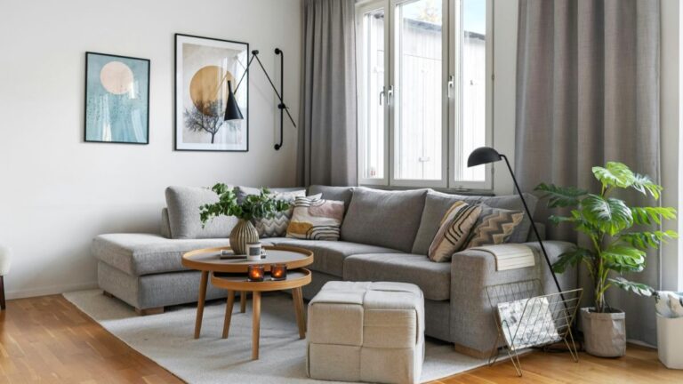 Sivá rohová pohovka, okrúhly drevený konferenčný stolík a jemný svetlý koberec v obývacej izbe.