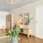 Svetlá obývacia izba so skleneným stolíkom, drevenou komodou a moderným lamelovým stropným svietidlom.