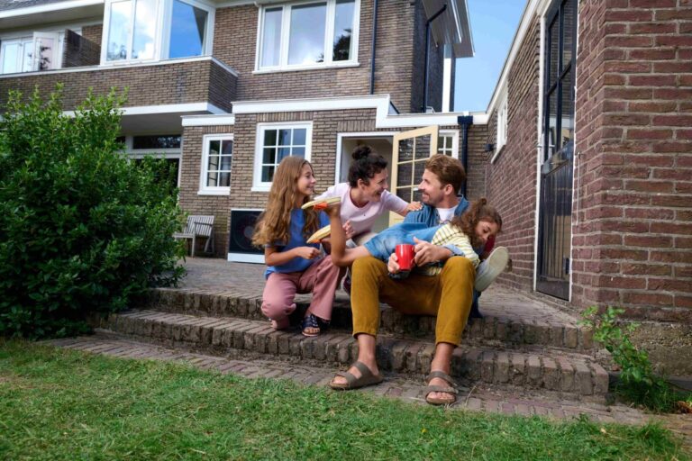 Rodina s dvoma dcérami na schodoch pri rodinnom dome s tehlovou fasádou.