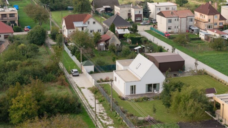 Biely rodinný dom so sedlovou strechou, nízkou bočnou časťou a oploteným pozemkom v zástavbe obce.