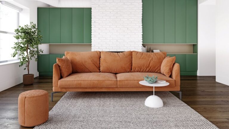 Obývačka s oranžovým gaučom, zelenými skrinkami a bielo-tehlovou stenou.