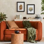 Spálňa s dreveným nočným stolíkom, svietiacou hríbovou lampou a béžovým čelom postele.