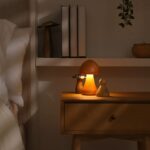 Spálňa s dreveným nočným stolíkom, svietiacou hríbovou lampou a béžovým čelom postele.