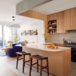 Moderná kuchyňa s masívnym dreveným ostrovom, svetlou kamennou doskou a sivým vrúbkovaným obkladom.