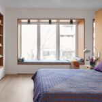 Spálňa s veľkou drevenou knižnicou, čalúneným okenným výklenkom a modrou vzorovanou prikrývkou.