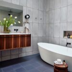 Kúpeľňa s voľne stojacou bielou vaňou, tmavomodrou dlažbou a drevenou skrinkou pod umývadlo.