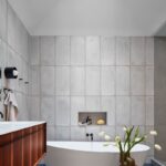 Kúpeľňa s vertikálnym sivým obkladom, oválnou bielou vaňou a dreveným dizajnovým stolíkom.