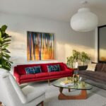 Obývacia izba s výraznou červenou pohovkou, skleneným konferenčným stolíkom a veľkým abstraktným obrazom.