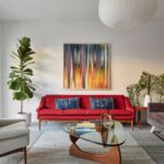 Obývacia izba s moderným červeným gaučom, dreveným trojuholníkovým stolíkom a abstraktným obrazom.