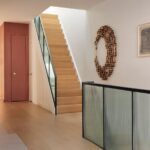 Chodba s čistým dreveným schodiskom, preskleným zábradlím a bronzovou nástennou plastikou.