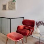 Interiér s luxusným červeným kreslom, drevenou podnožkou a skleneným príručným stolíkom.