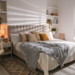 Svetlá spálňa s čalúnenou posteľou, horčicovými vankúšmi, bielymi vstavanými policami a vlneným krémovým kreslom.