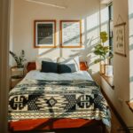 slnečná spálňa s drevenou posteľou, vzorovanou prikrývkou a dvoma zarámovanými čiernobielymi obrazmi na stene.