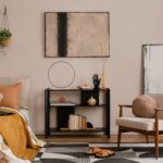 Moderná obývacia izba s béžovým kreslom, čiernym regálom, abstraktným obrazom a vzorovaným kobercom.