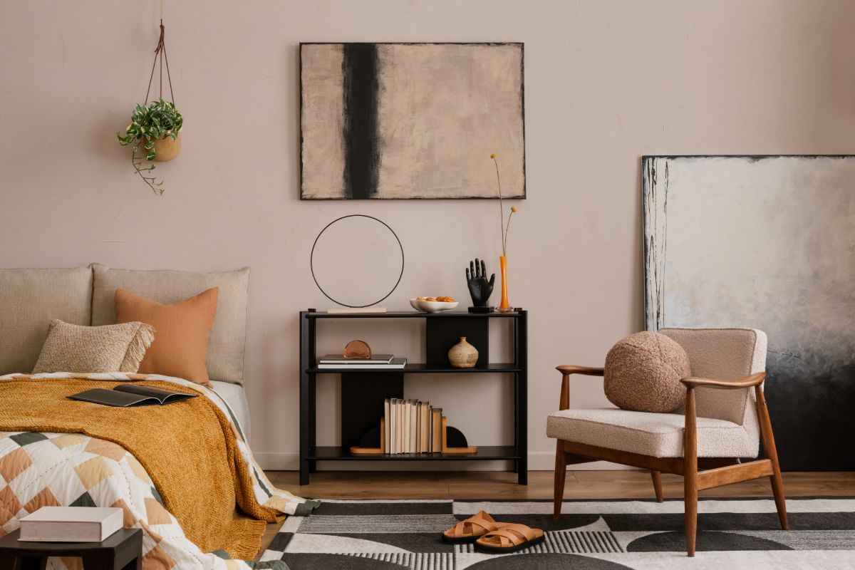 Moderná obývacia izba s béžovým kreslom, čiernym regálom, abstraktným obrazom a vzorovaným kobercom.