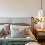 Detail spálne s čalúneným čelom postele, zelenými vankúšmi, dreveným nočným stolíkom a bielym visiacim svietidlom.