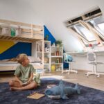 Chlapec sedí na koberci v podkrovnej izbe so strešnými oknami Velux.
