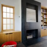 Obývacia izba s masívnym čiernym krbom, drevenou komodou, vstavanou knižnicou a červeným plastovým košom na drevo.