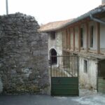 Exteriér s masívnym kamenným múrom, zelenou kovovou bránou a historickou vidieckou architektúrou.