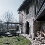 Exteriér s kamennou klenbou, historickou studňou, šedou omietkou a kovovým odkvapovým systémom.