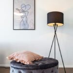 Taburet s úložným priestororm pri stojatej lampe v interiéri.