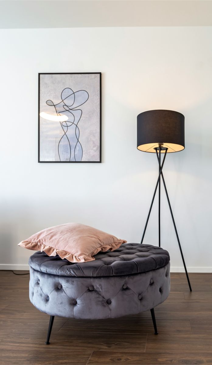 Taburet s úložným priestororm pri stojatej lampe v interiéri.