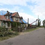 Starší rodinný dom s očmudenými stenami a poškodenou strechou, prekrytou modrou fóliou.