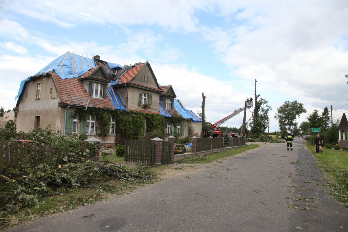 Starší rodinný dom s očmudenými stenami a poškodenou strechou, prekrytou modrou fóliou.