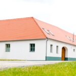Biely dom s červenou strechou a tyrkysovými oknami.