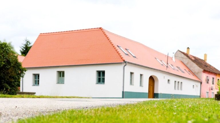 Biely dom s červenou strechou a tyrkysovými oknami.