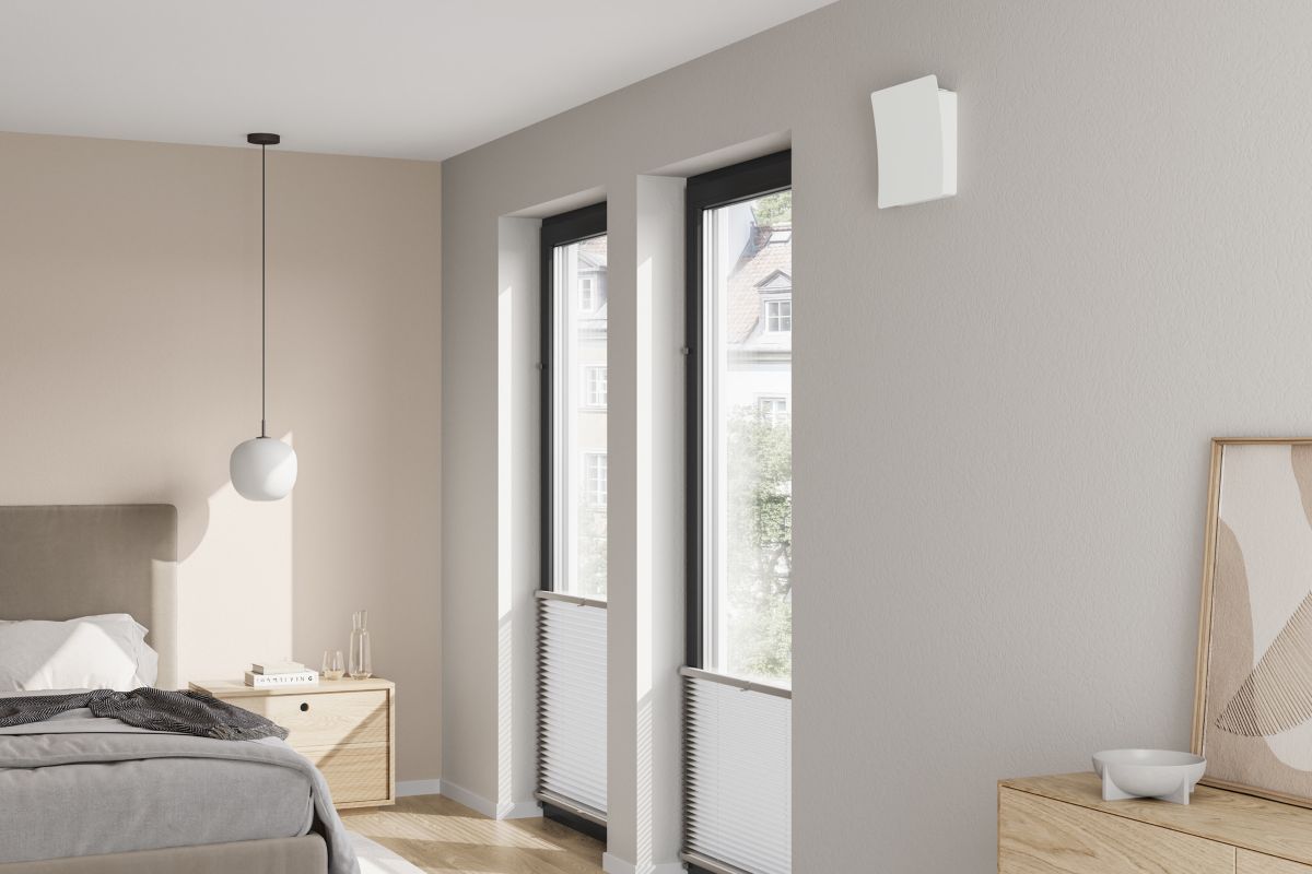 Moderná spálňa s vysokými oknami a rekuperačnou jednotnou Stiebel Eltron na stene.