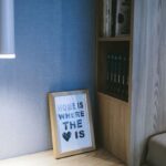 Drevená polica s knihami, svetlá vzorovaná tapeta, biele svietidlo a drevený fotorámik.