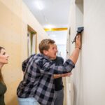 Mladí muž kontroluje prácu v rozostavanom interiéri spolu so ženou a druhým mužom.
