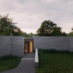 Exteriér moderného domu so sivým betónovým oplotením a štrkovým chodníkom.
